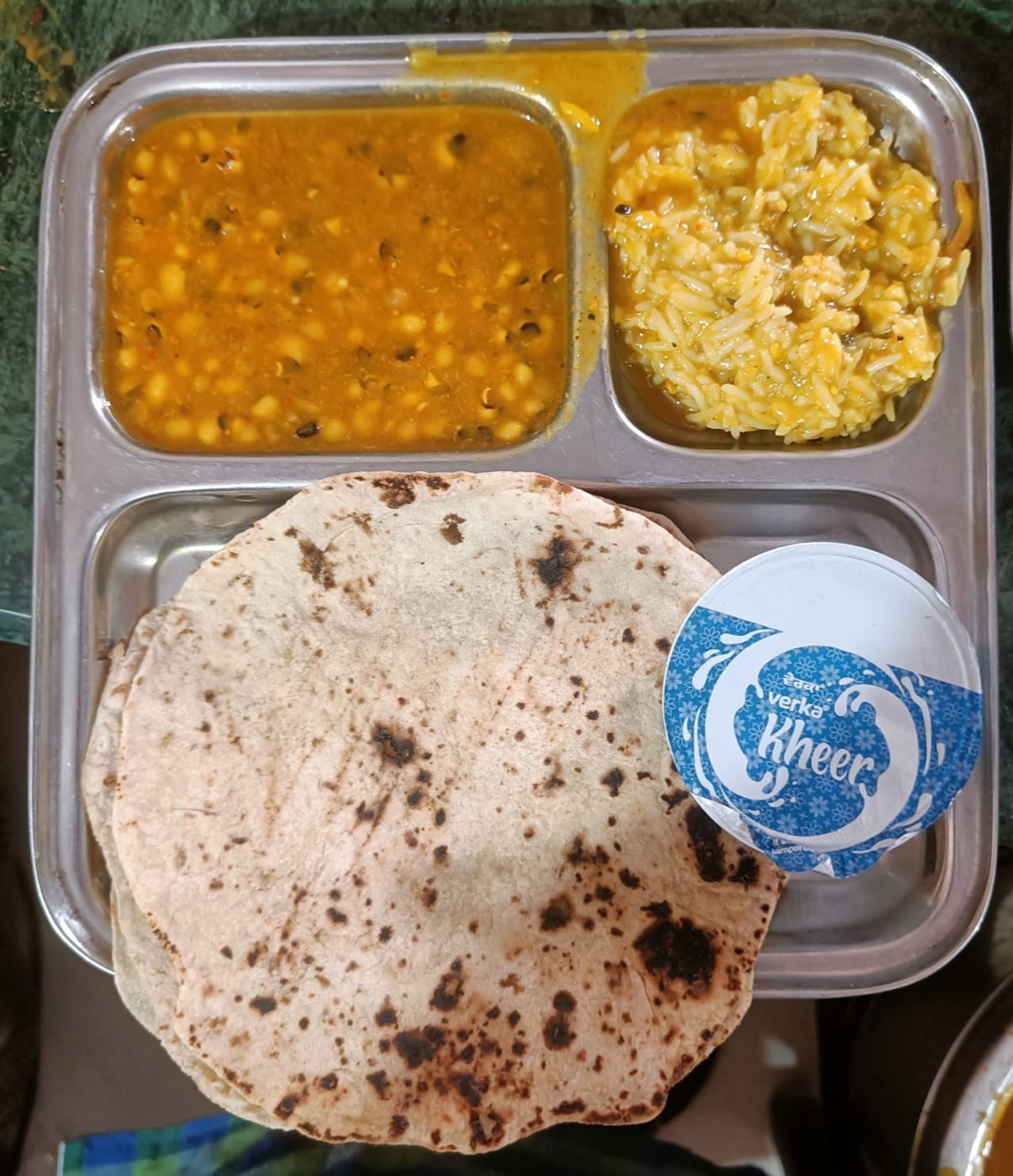 A steel tray of daal, rice, roti, and kheer