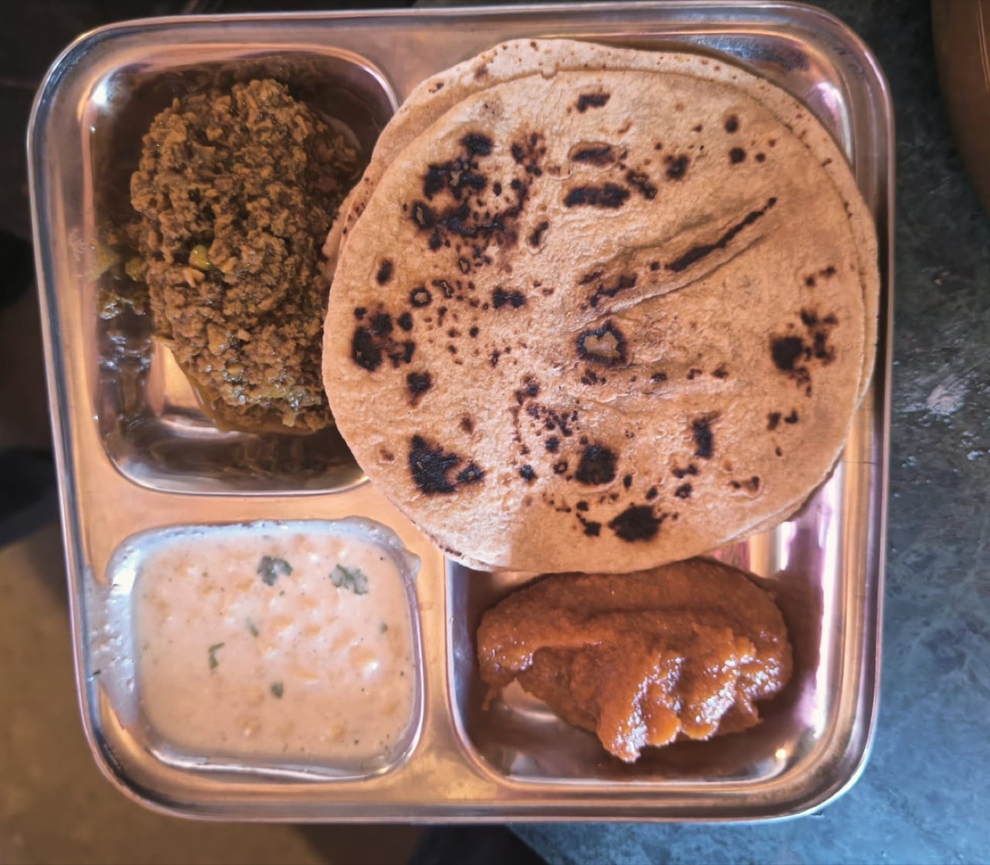 A steel plate with roti, sabzi, and dal