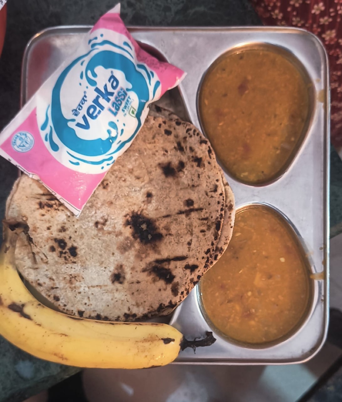 A meal tray with roti, daal, lassi, and a banana