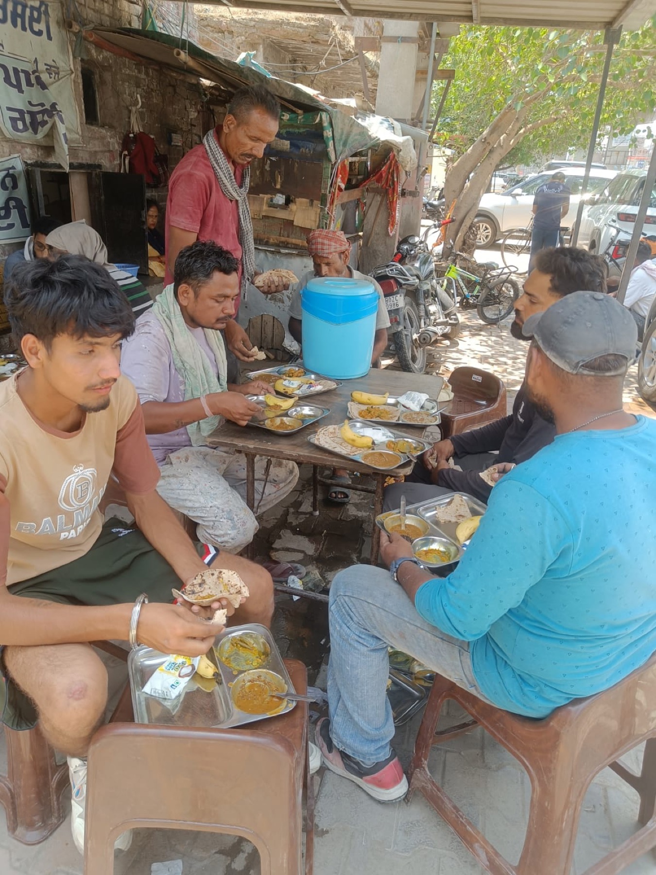 Beneficiaries sharing a meal together under a tree near Paavan Rasoi